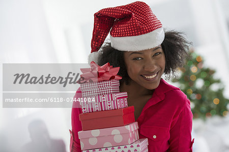 A woman wearing a red and white Father Christmas hat.  At home. A decorated Christmas tree.