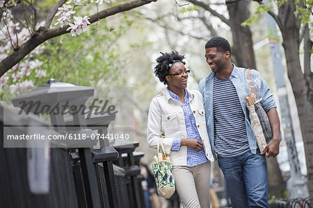 A couple walking in the park side by side carrying shopping bags.