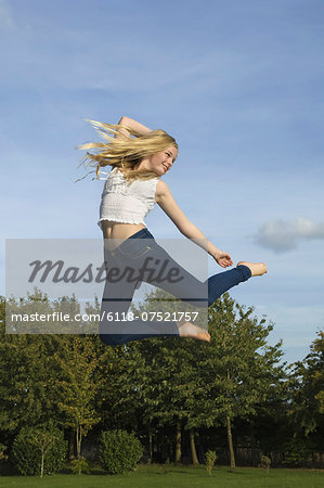 Teenage girl with long blond hair jumping in the air.