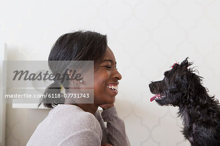 A young girl playing with her small black pet dog.