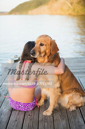 A young girl and a golden retriever dog sitting on a jetty.