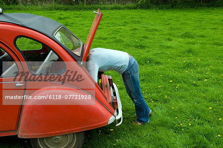 A person leaning in to the boot at the rear of the car. A person leaning in to the boot at the rear of the car.