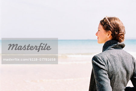 A woman in a grey jacket looking out over a beach and the sea.