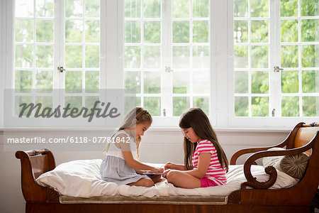 Two girls sitting and playing, using a digital tablet.