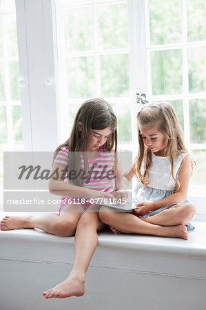 Two girls playing, sharing a digital tablet.