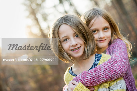 Two smiling girls in a forest, hugging each other.