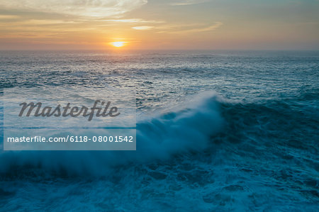 Sunset over crashing waves and surf. View out to the horizon.