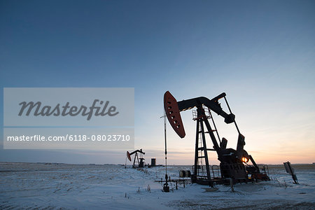 An oil drilling rig and pumpjack on a flat plain in the Canadian oil fields at sunset.