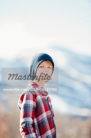 A boy with a woolly hat and checked shirt standing in open countryside in winter.