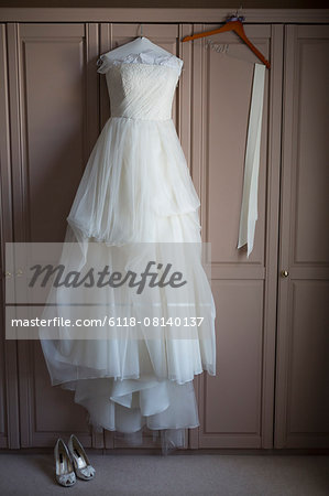 Wedding dress hanging on a wardrobe door, wedding shoes on the floor.