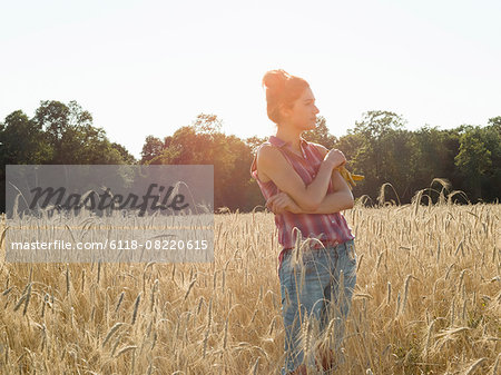 Young woman wearing a checked shirt standing in a cornfield.