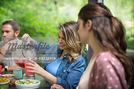 Three people seated at a table in woodland, having a meal, one woman pouring juice from a jug.