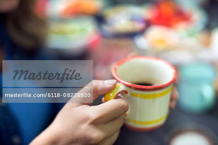 One person at a picnic table outdoors, holding a china mug.