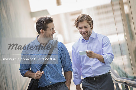 Two businessmen standing in an urban street, using smart phones.