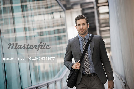 A man carrying a computer bag with a strap on a city walkway.
