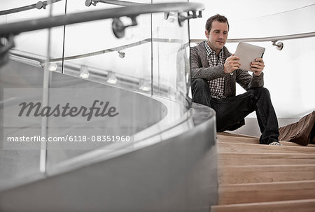 A man seated on steps using a digital tablet.
