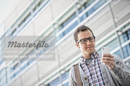 A man in a checked shirt with open collar holding his smart phone.