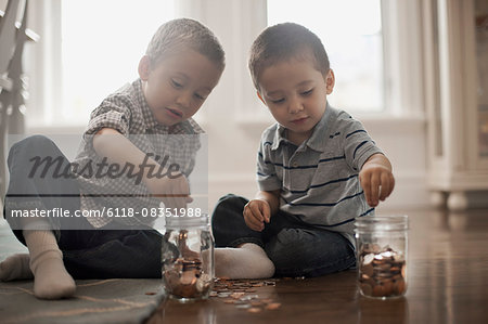 Two children playing with coins, dropping them into glass jars.