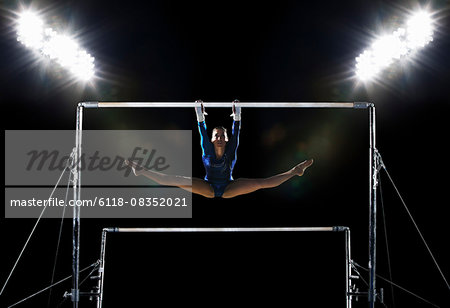 A female gymnast, a young woman performing on the parallel bars performing, with legs extended.