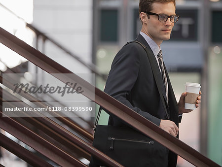 A working day. Businessman in a work suit and tie walking down steps holding a cup of coffee.