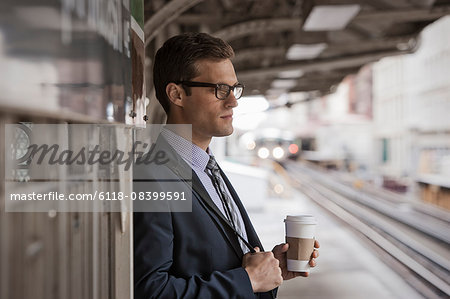 A working day. Businessman in a work suit and tie holding a cup of coffee on a railway platform.