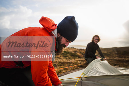 Two men holding and putting up a small tent in open space. Wild camping.