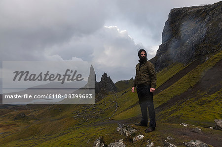 A man on a narrow path rising to a dramatic landscape of rock pinnacles under an overcast sky with low cloud.