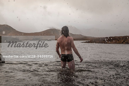 A man standing thigh deep in sea water in swimming trunks.