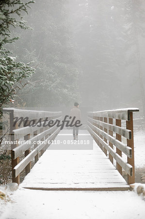 A woman walking on a footbridge in the mountains in snow.