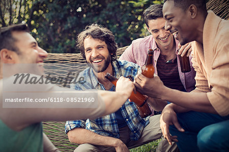 A group of friends lounging in a large hammock in the garden having a beer.