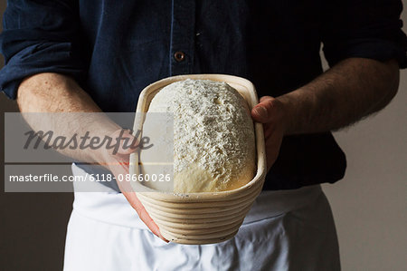 Close up of a baker holding a freshly baked loaf of white bread in a rattan proofing basket.