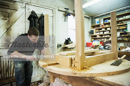 A man in a carpentry workshop, working on the edge of a new wooden table using a hammer.