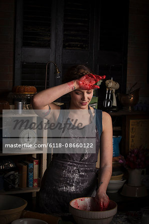 Valentine's Day baking, young woman standing in a kitchen, preparing raspberry jam, wiping her hand on her forehead.