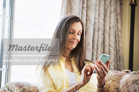 Senior woman with long brown hair sitting on a sofa, using a mobile phone.