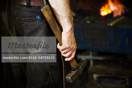 A man in a leather apron holding a hammer in a workshop.