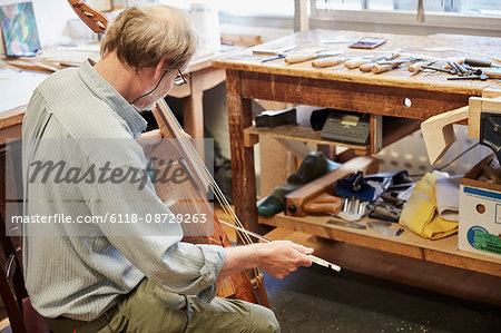 A violin maker in his workshop playing an instrument with a bow, tuning and finishing.