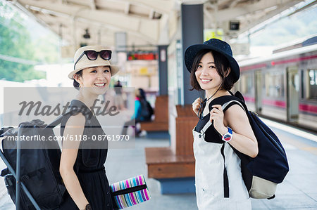 Two young women standing on a platform at a railway station.