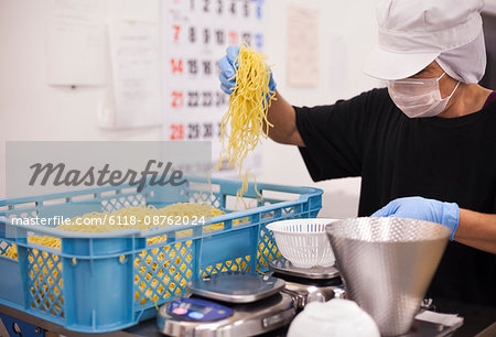 Workers in aprons and gloves weighing and packing freshly made noodles in a soba noodle production unit.