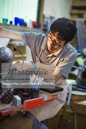 A craftsman at work in a glass maker's workshop, using a machine to etch glass.