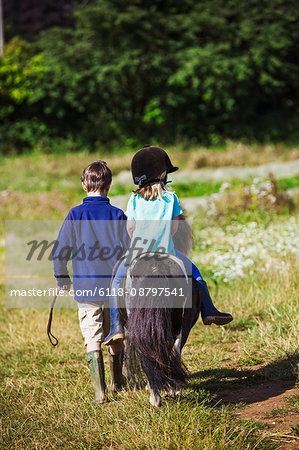 Download A Girl Riding A Pony And A Boy Walking Through A Field Stock Photo Masterfile Premium Royalty Free Code 6118 08797541
