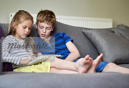 Two children seated sharing a digital tablet watching the screen.
