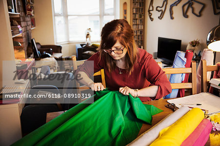 A woman ripping brightly coloured material on a tabletop in a workroom.