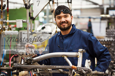 Male skilled factory worker with a partly assembled bicycle frame in a factory.