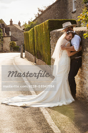 Newlyweds standing outdoors on a pavement, hugging and smiling.