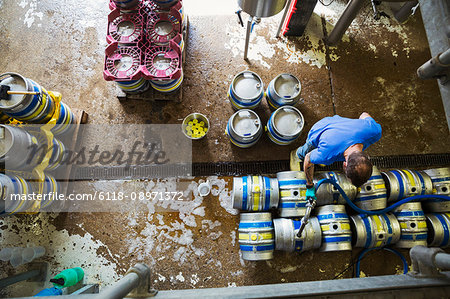 Directly above view of a man working in a brewery, metal beer kegs standing on the floor.