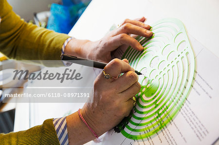 Close up of woman sitting at a drawing board, drawing with a fine liner pen, using a design template.