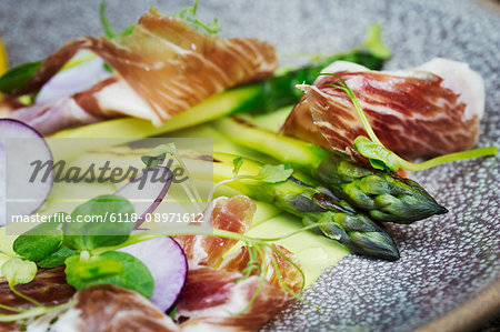 Close up high angle view of green asparagus and ham on a plate. A restaurant dish.