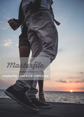 Low angle shot of two people dancing on a sea wall in front of the ocean.