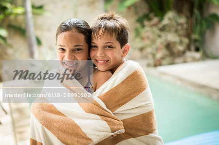 A boy and girl wrapped in a towel and cuddling.