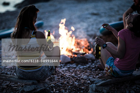 A group of young people gathered on a beach around a campfire..